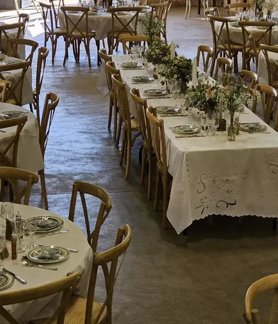 Salle de réception dressée : longues tables nappées, chaises en bois, bouquets champêtres