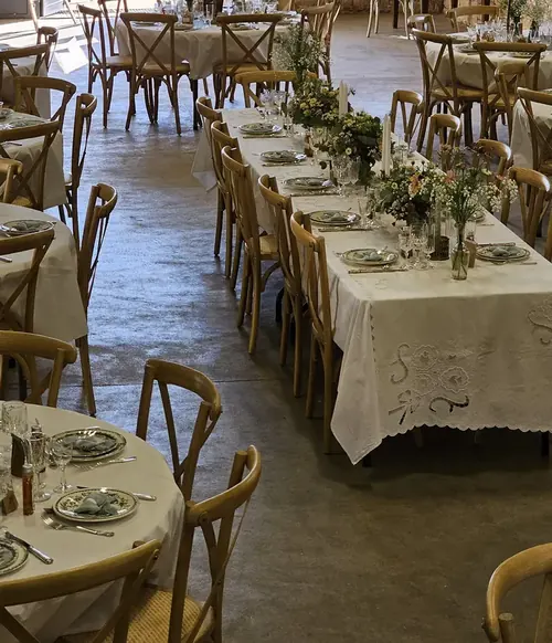 Salle de réception dressée : longues tables nappées, chaises en bois, bouquets champêtres